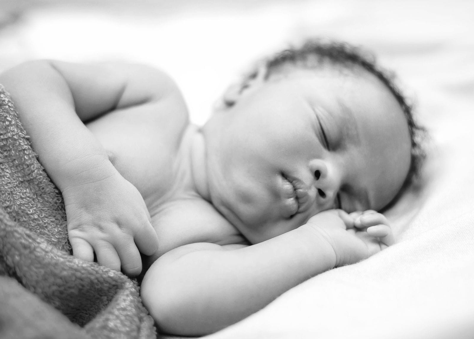 Un bébé endormi, les yeux fermés et les mains près du visage.