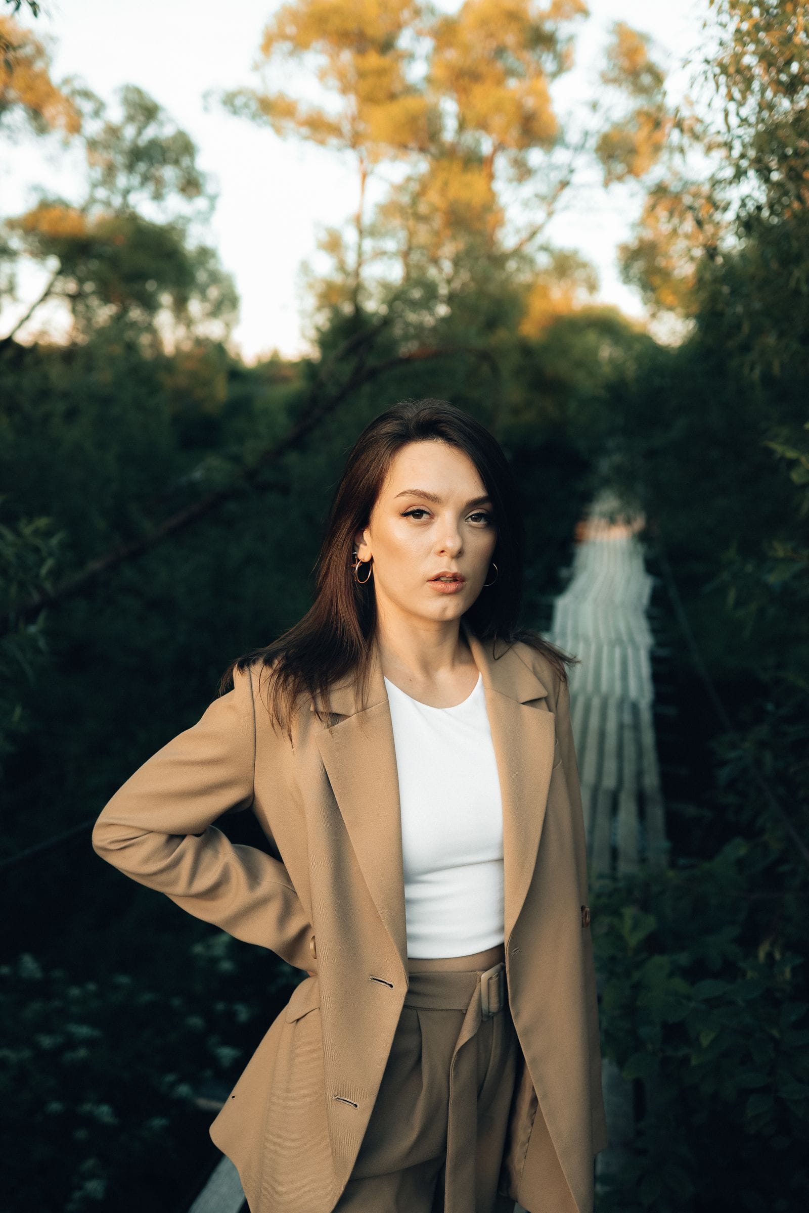Une femme en tenue beige, debout dans un environnement naturel, le regard assuré.